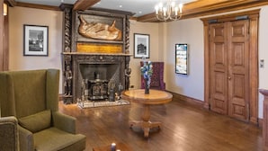 Une pièce avec une cheminée, un fauteuil vert, une table ronde en bois ornée de bougies et une porte en bois.