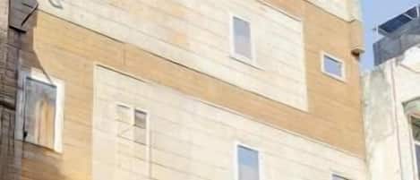 Un edificio de varios pisos con fachada color beige, varias ventanas y un escaparate con persiana cerrada.