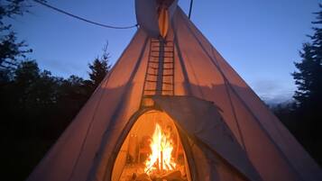 Un tipi avec un feu allumé à l’intérieur, entouré d’arbres.