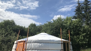 A traditional yurt with a white and blue patterned door, set on a wooden platform in a forested area.