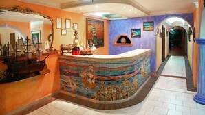A lobby with a curved reception desk, a ceiling fan, and a mural depicting a maritime scene. - Baluarte Cartagena Hotel Boutique (Cartagena)