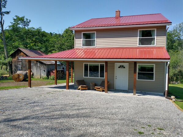 A two-story house with a red roof, a covered porch, and a gravel driveway. - Heydt Homestead (Seneca Rocks)