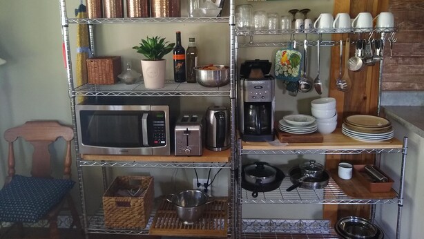 Una cucina con ripiano in acciaio inossidabile che contiene stoviglie, un forno a microonde, un tostapane e una macchina da caffè.