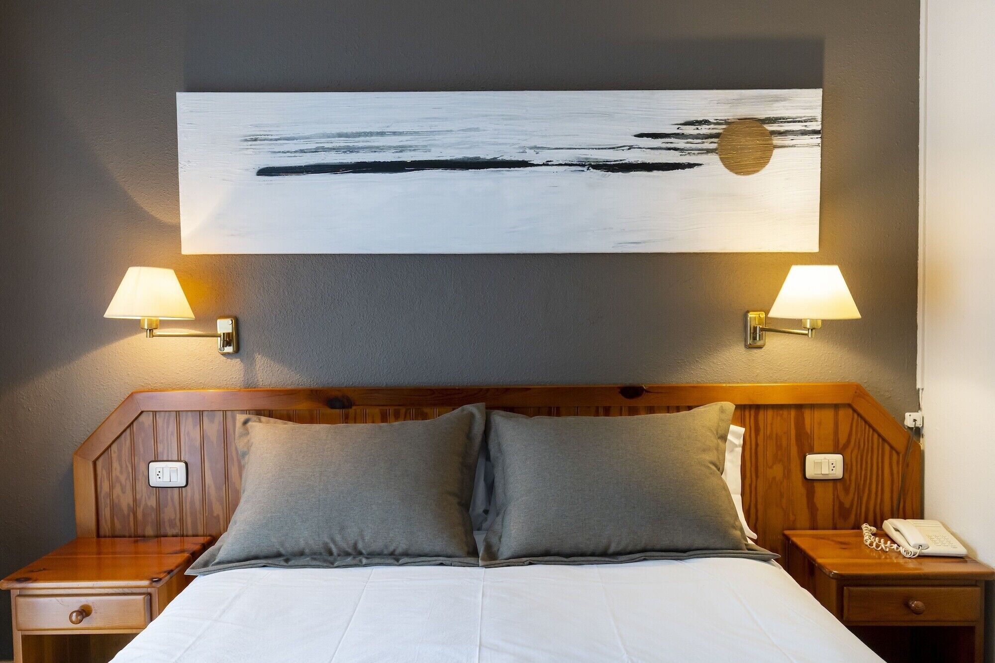 Habitación de hotel con cama, dos lámparas de noche, mesita con teléfono y un cuadro en la pared.