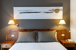 Habitación de hotel con cama, dos lámparas de noche, mesita con teléfono y un cuadro en la pared.