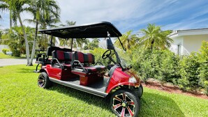A red golf cart parked on a well-maintained lawn with palm trees and a white building in the background.
