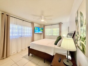 A hotel room with a bed, a television, a ceiling fan, and a window with curtains.