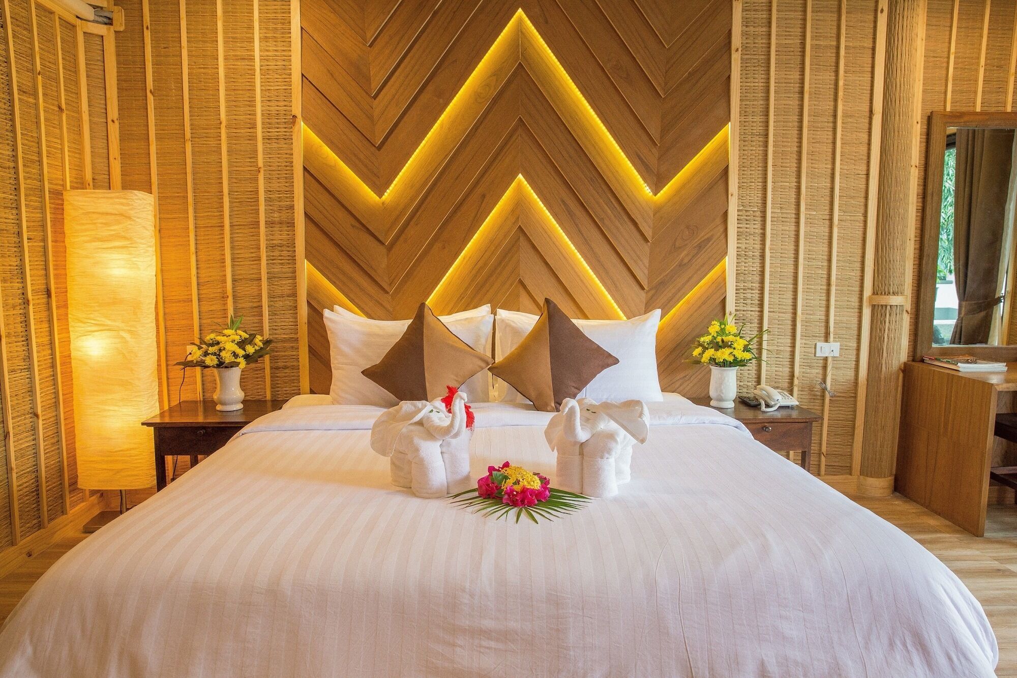 Habitación de hotel con una cama grande, panel de pared de madera y una mesita de noche con lámpara y flores.