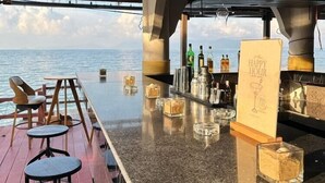A bar area with a view of the sea, wooden furniture, and a bar counter with bottles and glasses. - Adarin Beach Resort (Koh Samui)