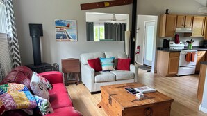 A cozy living room with a red sofa, a white couch, and a wooden coffee table. There's a kitchen area with wooden cabinets and a stove.