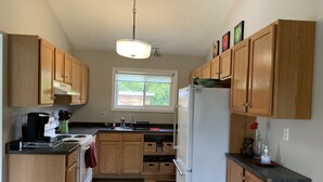 A kitchen with wooden cabinets, a white refrigerator, a coffee maker, and a window with a view of greenery outside.