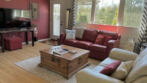 A living room with a red couch, a wooden coffee table, a television, and a window with curtains.