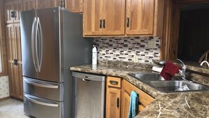A kitchen with wooden cabinets, a stainless steel refrigerator, a dishwasher, a sink, and a tiled backsplash. - Super Spacious Lakehome (Richmond)