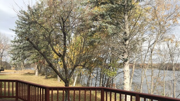 A wooden deck with a railing overlooking a lake, surrounded by trees with autumn foliage. - Super Spacious Lakehome (Richmond)