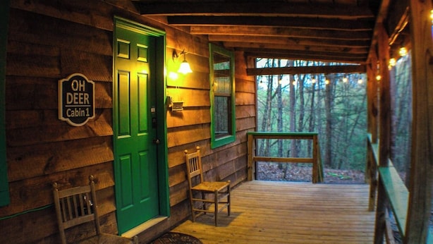 A cabin with a green door, a sign reading "OH DEER Cabin 1", and a wooden porch with a bench. - Oh Deer - Studio Wooded Twin Cabin, Hot Tub, TV & Wifi (Sevierville)