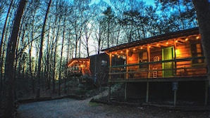 A rustic cabin with a porch and string lights, surrounded by trees. - Oh Deer - Studio Wooded Twin Cabin, Hot Tub, TV & Wifi (Sevierville)