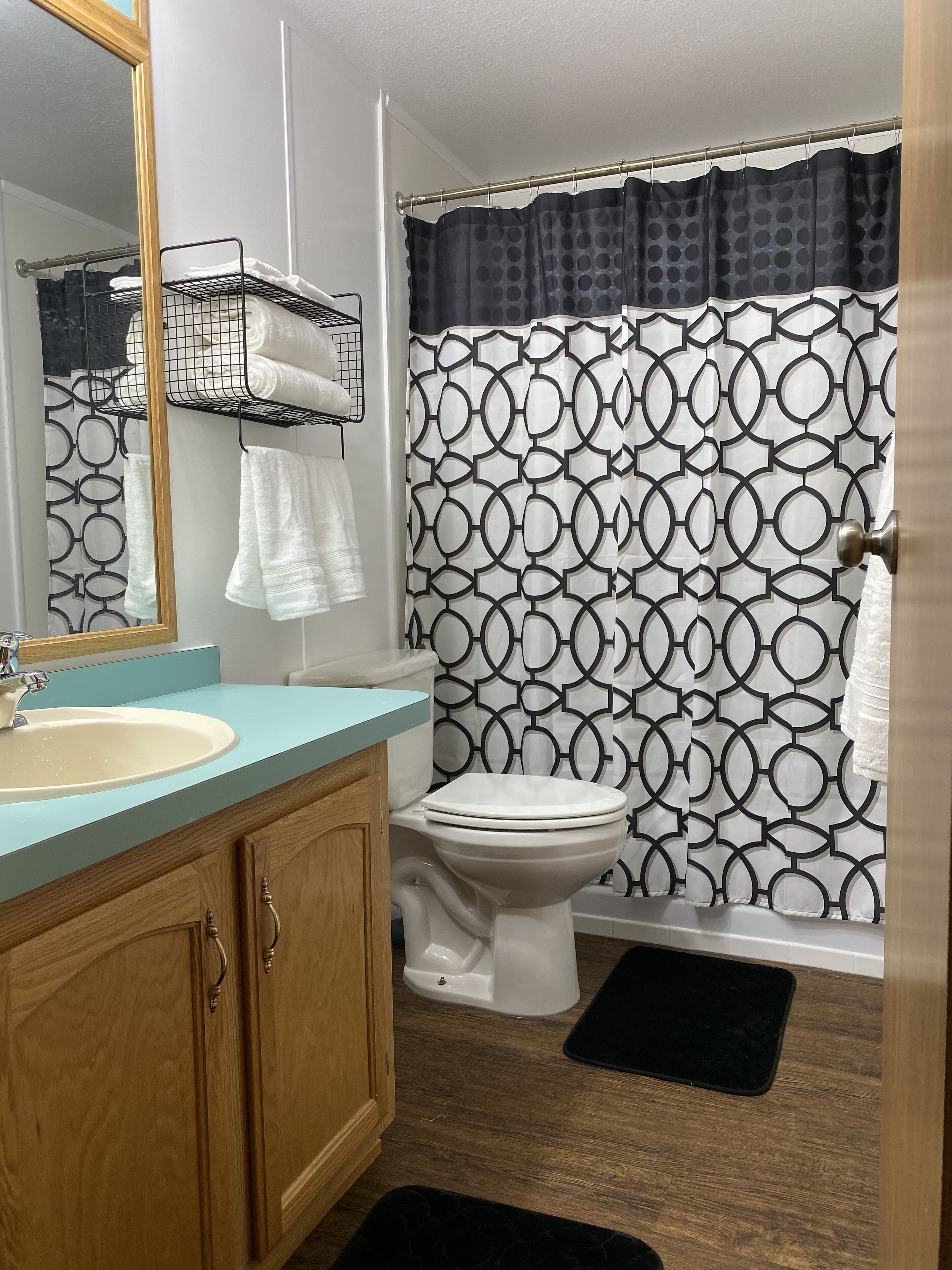 A bathroom with a white sink, wooden cabinets, a toilet, and a shower curtain with a geometric pattern.
