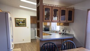 Una cocina compacta con gabinetes de madera, microondas integrado y un comedor con mesa y sillas de madera.