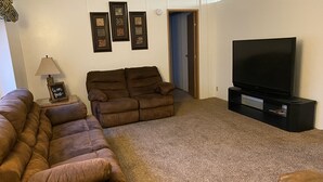 Una sala de estar con un sofá marrón, un televisor y cuadros enmarcados en la pared.