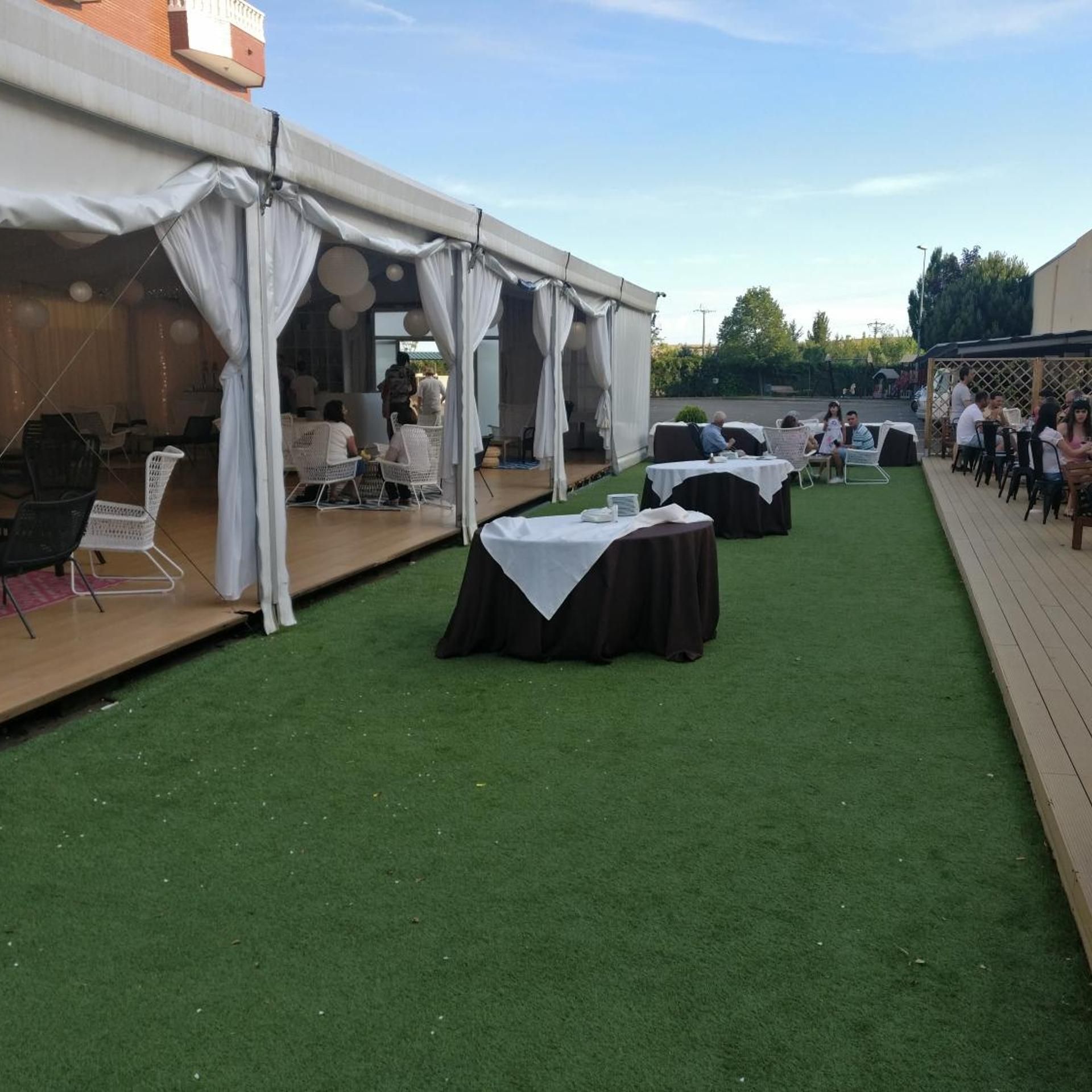 Un espacio al aire libre para eventos con mesas, sillas, una zona cubierta y un césped.