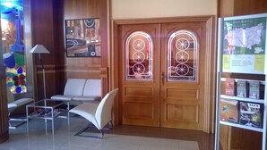 A hotel reception area with a modern design, featuring a reception desk, two waiting chairs, and a glass display case with brochures. - Hotel Camino Real (Valdefresno)