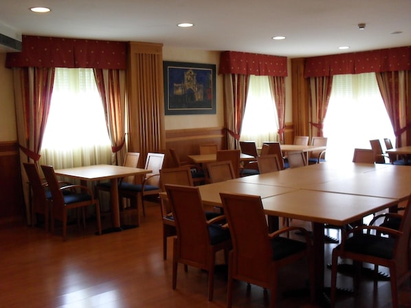 A conference room with wooden tables and chairs, large windows with curtains, and a painting on the wall. - Hotel Camino Real (Valdefresno)