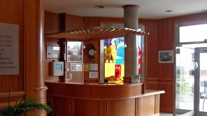 A reception area with a wooden counter, a clock, a stained glass window, and a door leading outside. - Hotel Camino Real (Valdefresno)