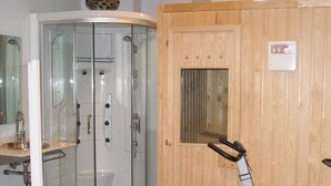 A room with a glass-enclosed shower, wooden door, exercise equipment, and a sink with a mirror. - Hotel Camino Real (Valdefresno)