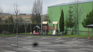 A parking lot with a playground area, including swings and slides, adjacent to a green building. - Hotel Camino Real (Valdefresno)
