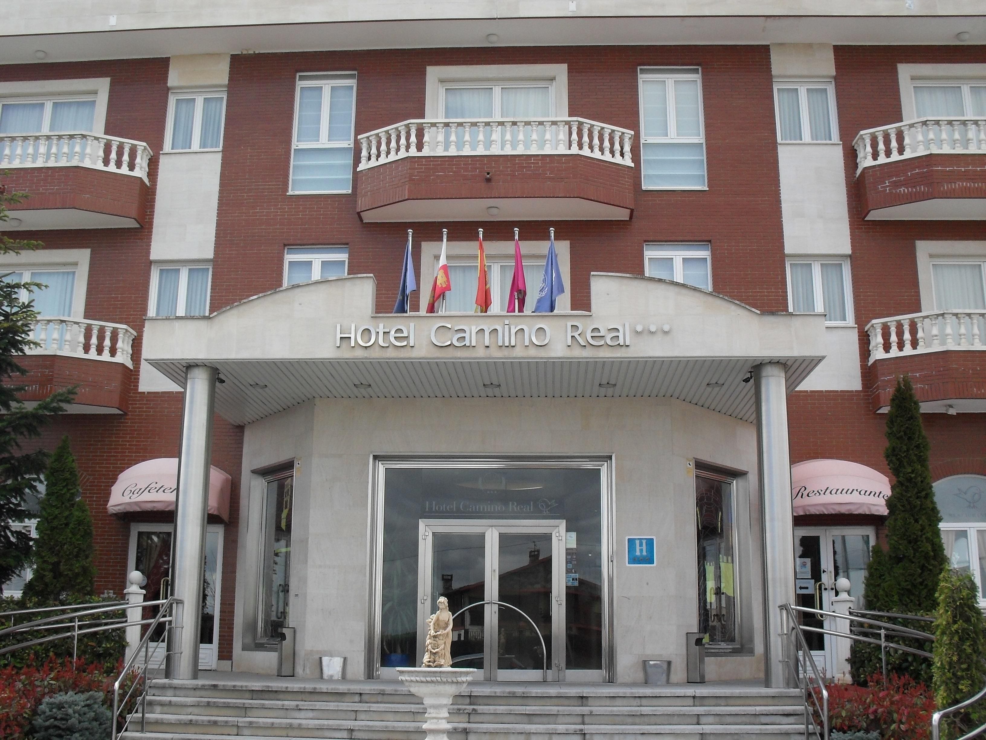 Hotel Camino Real con entrada principal, exhibici ón de banderas y una estatua al frente.