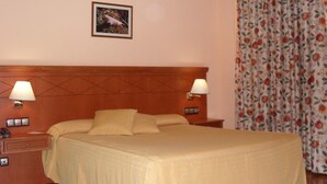 A hotel room with a large bed, two bedside lamps, a nightstand, a power outlet, and a floral curtain. - Hotel Camino Real (Valdefresno)