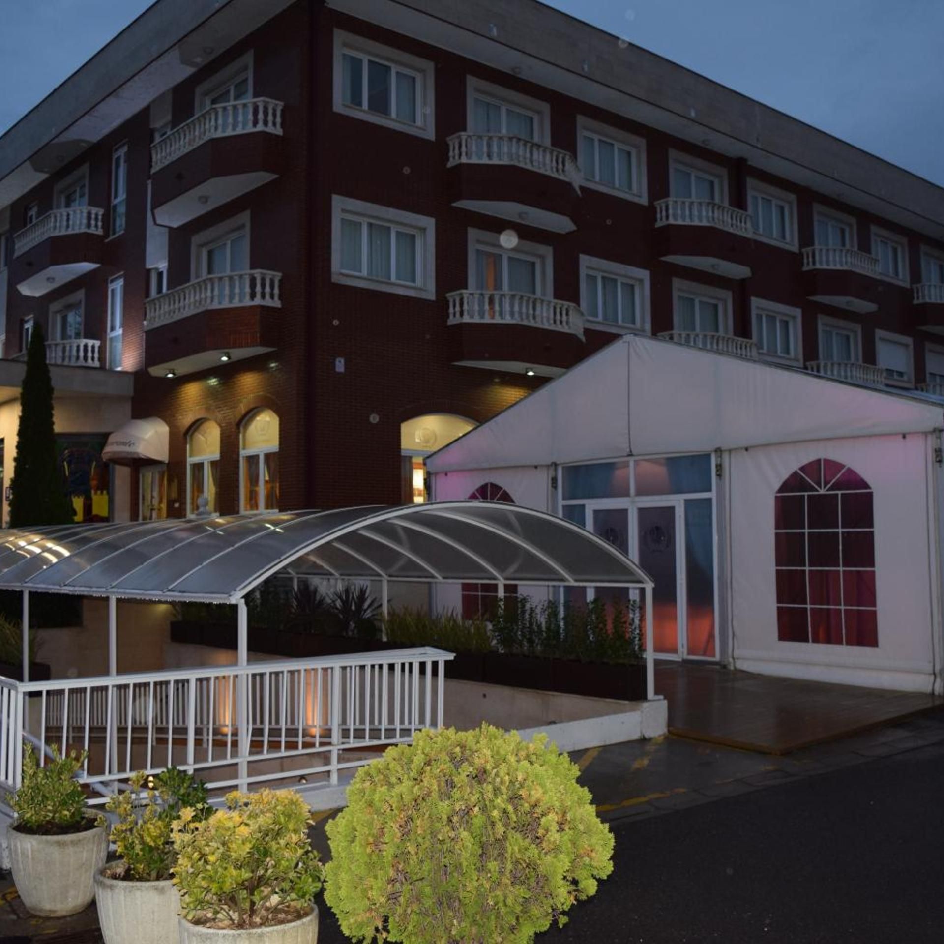 A multi-story hotel with a covered outdoor seating area and a white building adjacent to it.