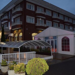A multi-story hotel with a covered outdoor seating area and a white building adjacent to it. - Hotel Camino Real (Valdefresno)