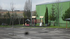 A parking lot with a playground area, including swings and slides, adjacent to a green building. - Hotel Camino Real (Valdefresno)