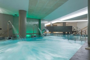 An indoor swimming pool with multiple water jets, a tiled floor, and a modern architectural design. - Spa Sercotel Odeon (Naron)