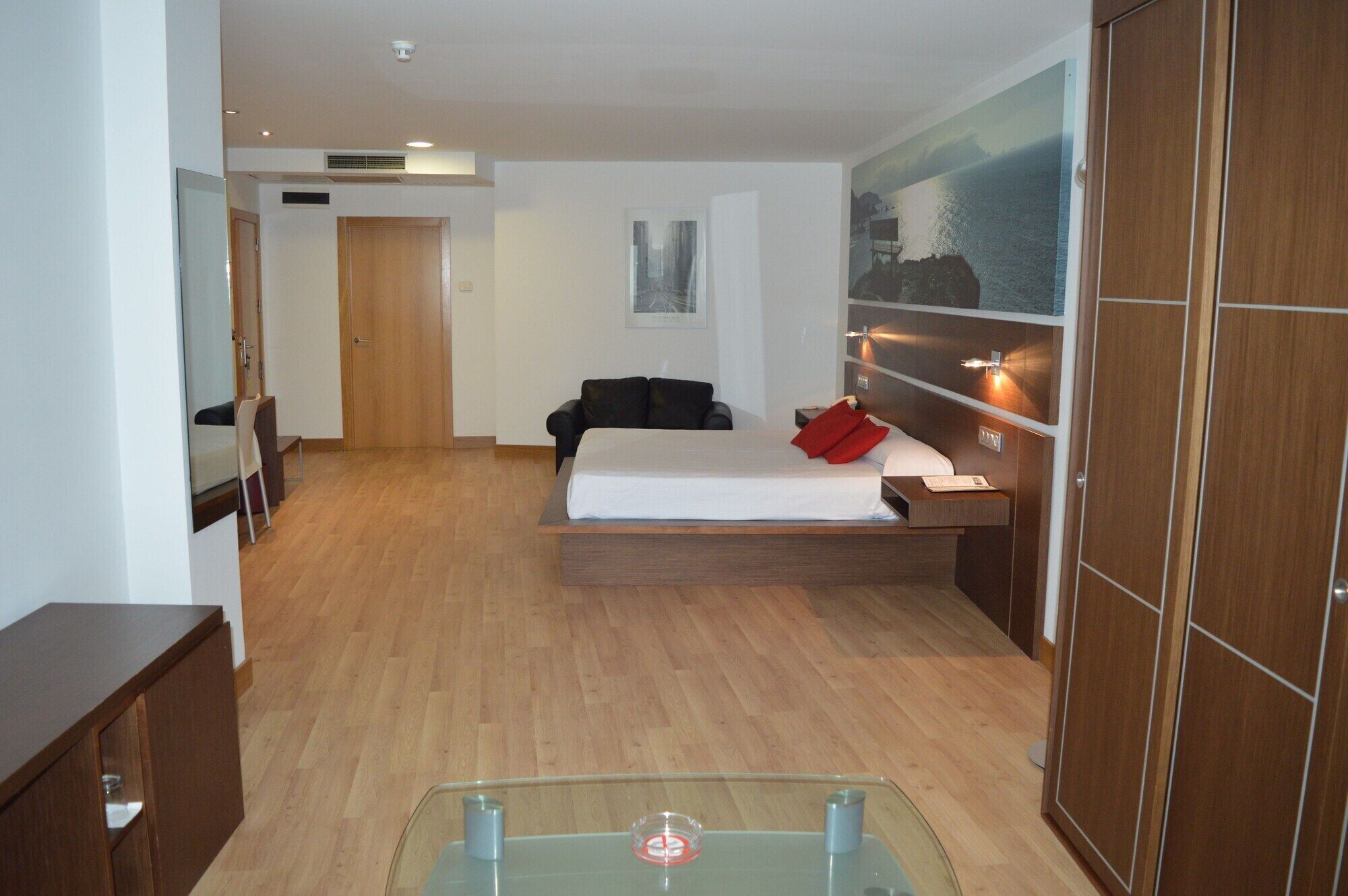 A modern hotel room with a bed, a desk, a chair, and a wardrobe.