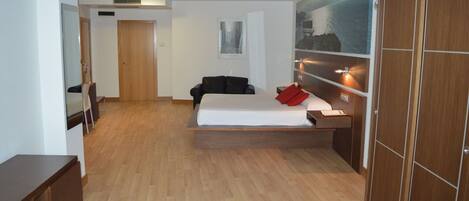 A modern hotel room with a bed, a desk, a chair, and a wardrobe.
