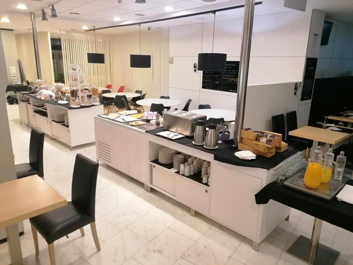 A modern hotel dining area with a central counter, multiple tables, and chairs.