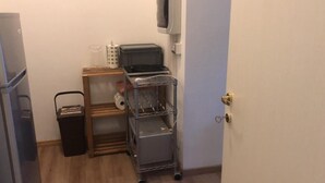 Une petite cuisine équipée d’un réfrigérateur, d’un four à micro-ondes, d’un évier et d’un chariot métallique à étagères.