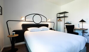 Une chambre d’hôtel comprenant un lit, une table de chevet, une lampe et un bureau avec une chaise.