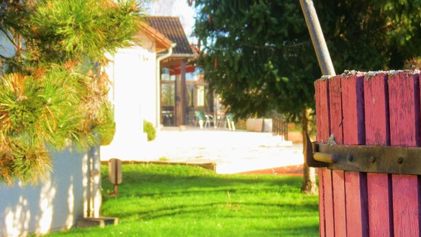 A red wooden fence with a metal gate, a grassy lawn, and a building with a tiled roof in the background. - Kyriad Nuits-saint-georges (Nuits-Saint-Georges)