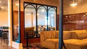 A cozy lounge area with a sofa and chairs, a patterned rug, and a glass partition with a view of a bar area. - Kyriad Nuits-saint-georges (Nuits-Saint-Georges)