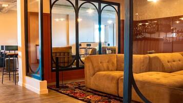 Un espace salon confortable avec un canapé et des fauteuils, un tapis à motifs et une cloison en verre donnant sur un bar.