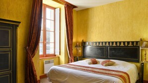Slaapkamer met een groot bed, een raam met gordijnen, een radiator en een hoofdbord met decoratieve details.