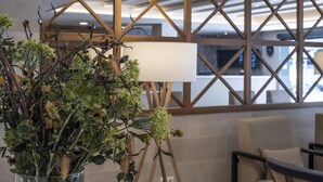 Un área de recepción con una planta grande en maceta, un espacio de descanso con sofá y sillones, y un separador de madera con un panel blanco.