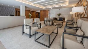 Un moderno vestíbulo de hotel con mostrador de recepción, zona de estar e iluminación empotrada en el techo.