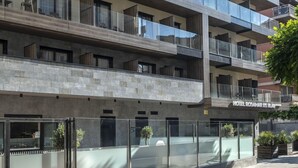 Un hotel moderno con fachada de vidrio, varios balcones y exterior con textura de piedra.