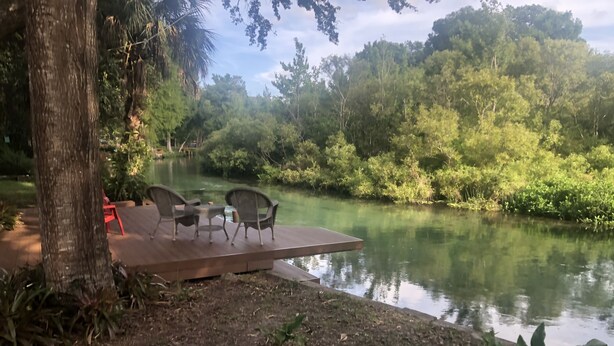 A riverside deck with outdoor furniture and a view of the river and surrounding greenery. - Weeki Wachee MAIN RIVER (Spring Hill)