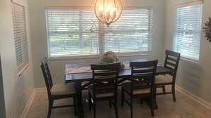 A dining area with a table and chairs, a chandelier, and windows with blinds. - Weeki Wachee MAIN RIVER (Spring Hill)