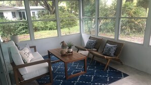A sunlit room with a large window, a wooden table, two wicker chairs, and a blue patterned rug. - Weeki Wachee MAIN RIVER (Spring Hill)